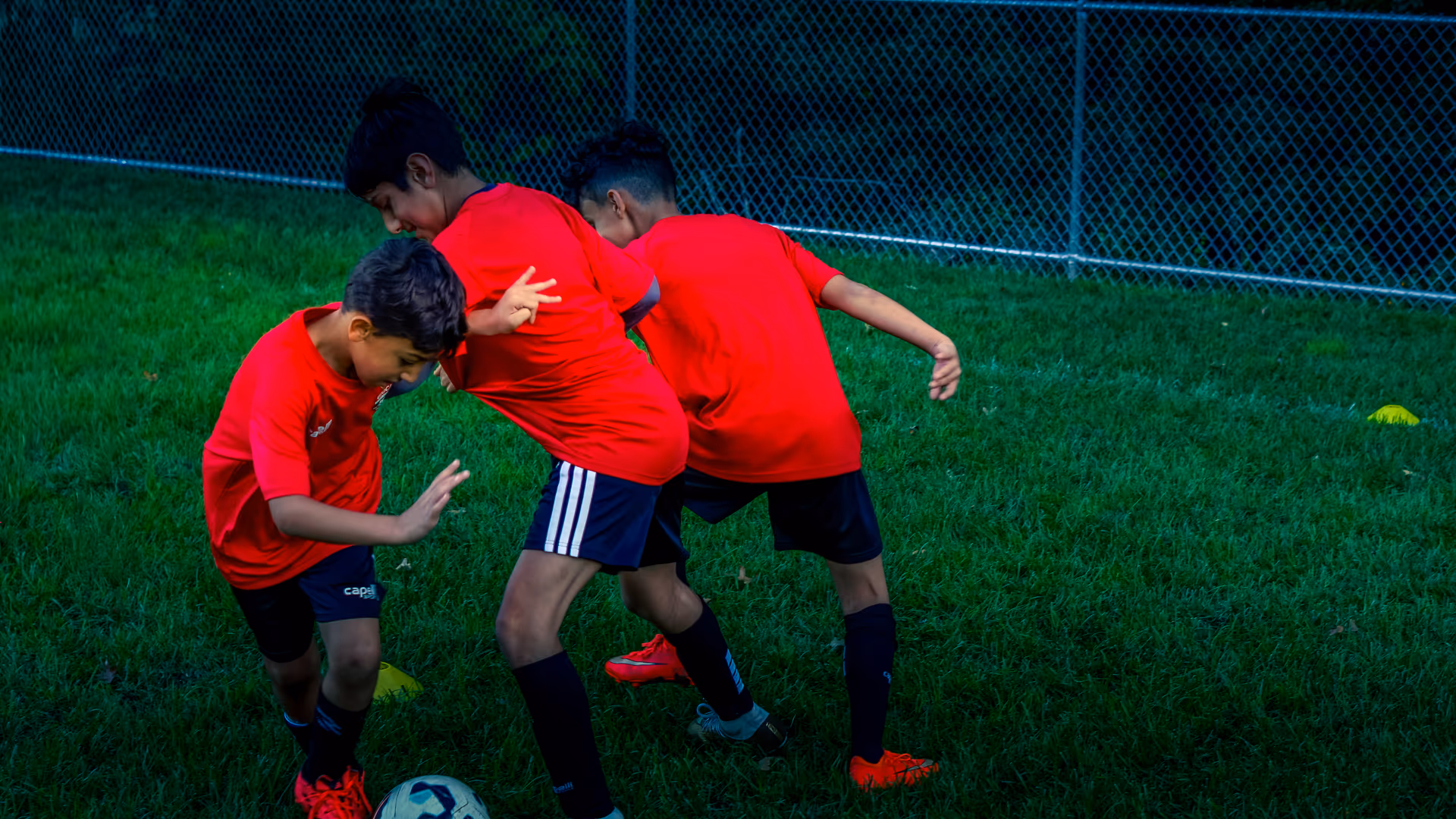 Three Gioca players in red shirts battling for the ball in a close shielding drill