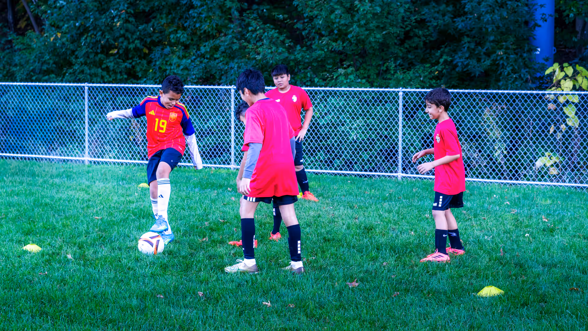 A young player rolling the ball under his sole while teammates in red Gioca shirts look on